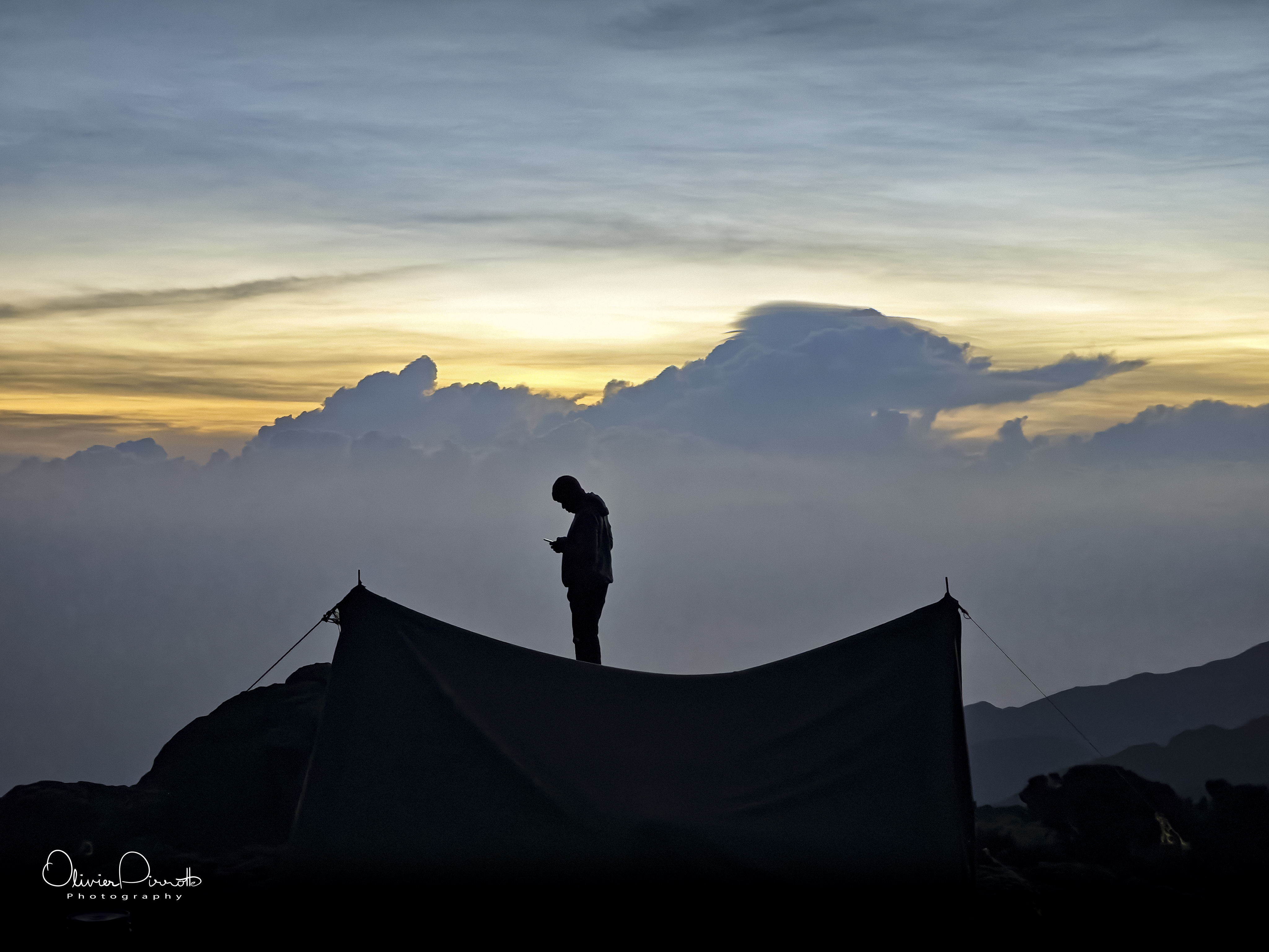 Silhouette of a person standing above a tent at dusk